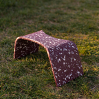 A small arched poop stool with a reddish-brown speckled pattern, placed on a grassy lawn outdoors.
