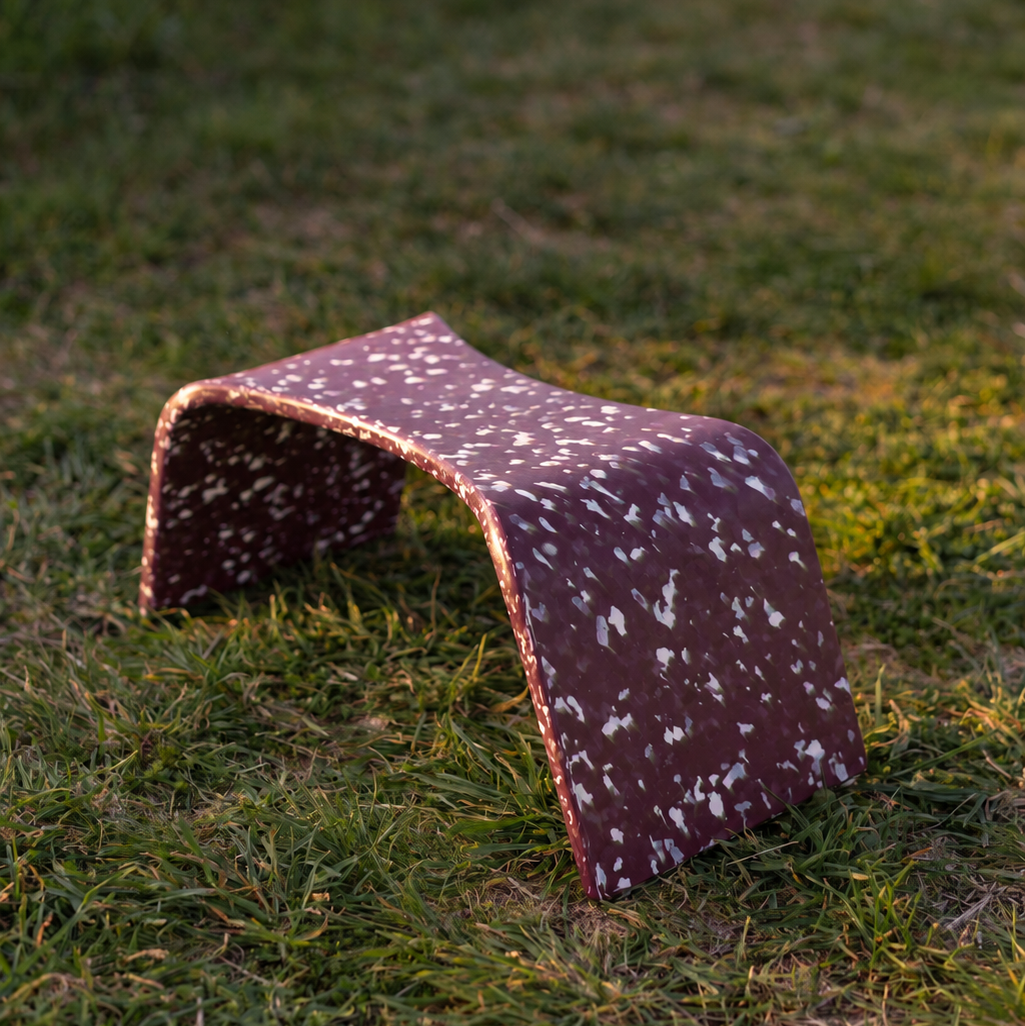 A small arched poop stool with a reddish-brown speckled pattern, placed on a grassy lawn outdoors.