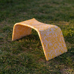 A yellow and white checkered bathroom stool on grass, designed to be placed over a toilet for ease of use.