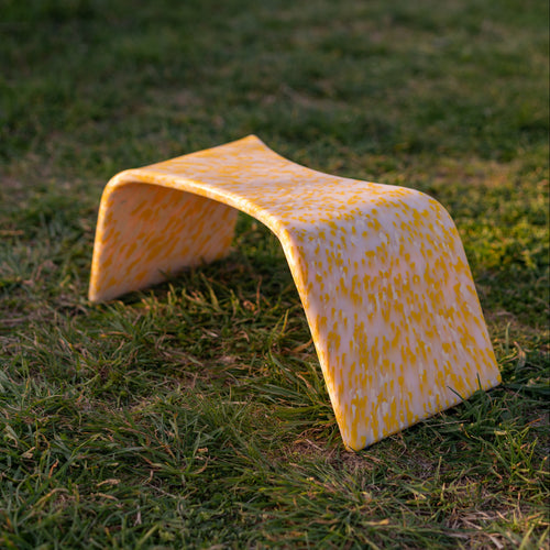 A yellow and white checkered bathroom stool on grass, designed to be placed over a toilet for ease of use.
